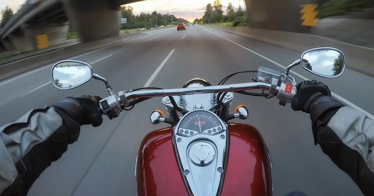 First-person POV of motorcycle riding - hands gripping handlebars while cruising down an open road